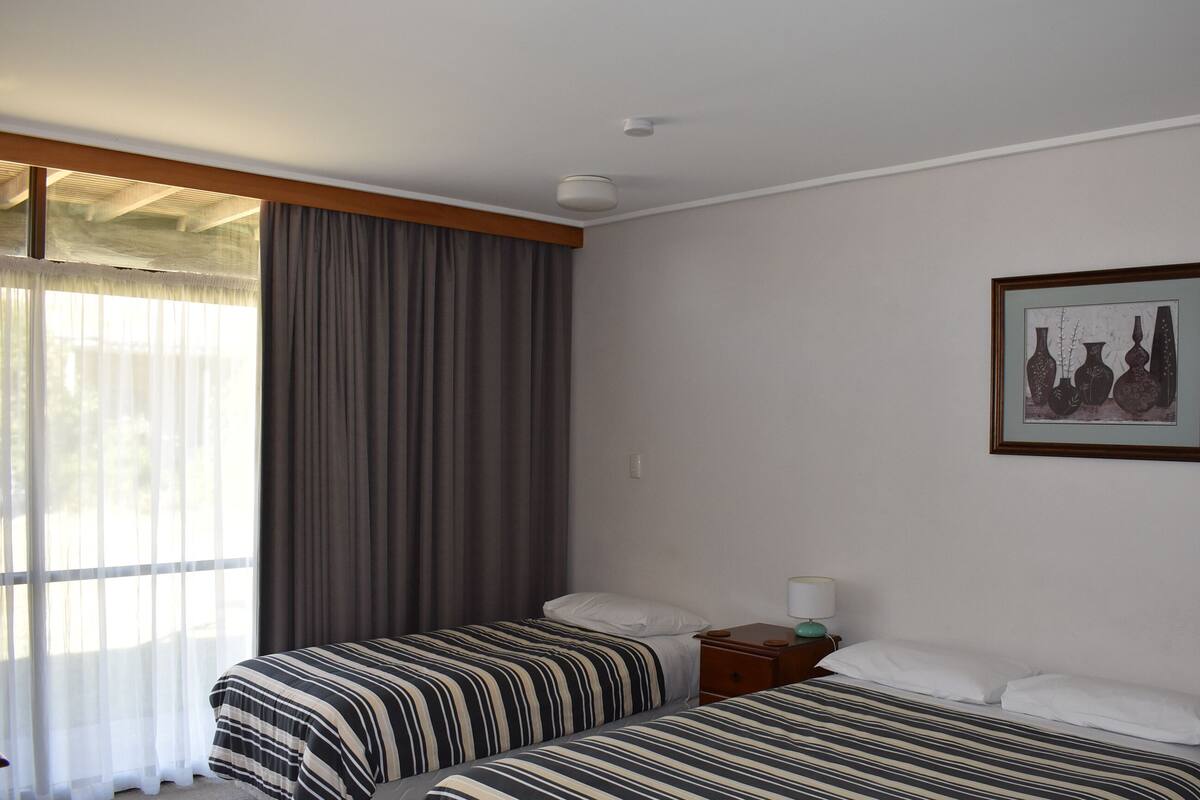 A hotel room with two beds, a nightstand, a lamp, and a framed picture on the wall.