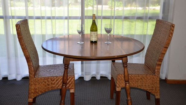 Una mesa redonda de madera con dos sillas de mimbre, una botella de vino y dos copas de vino.