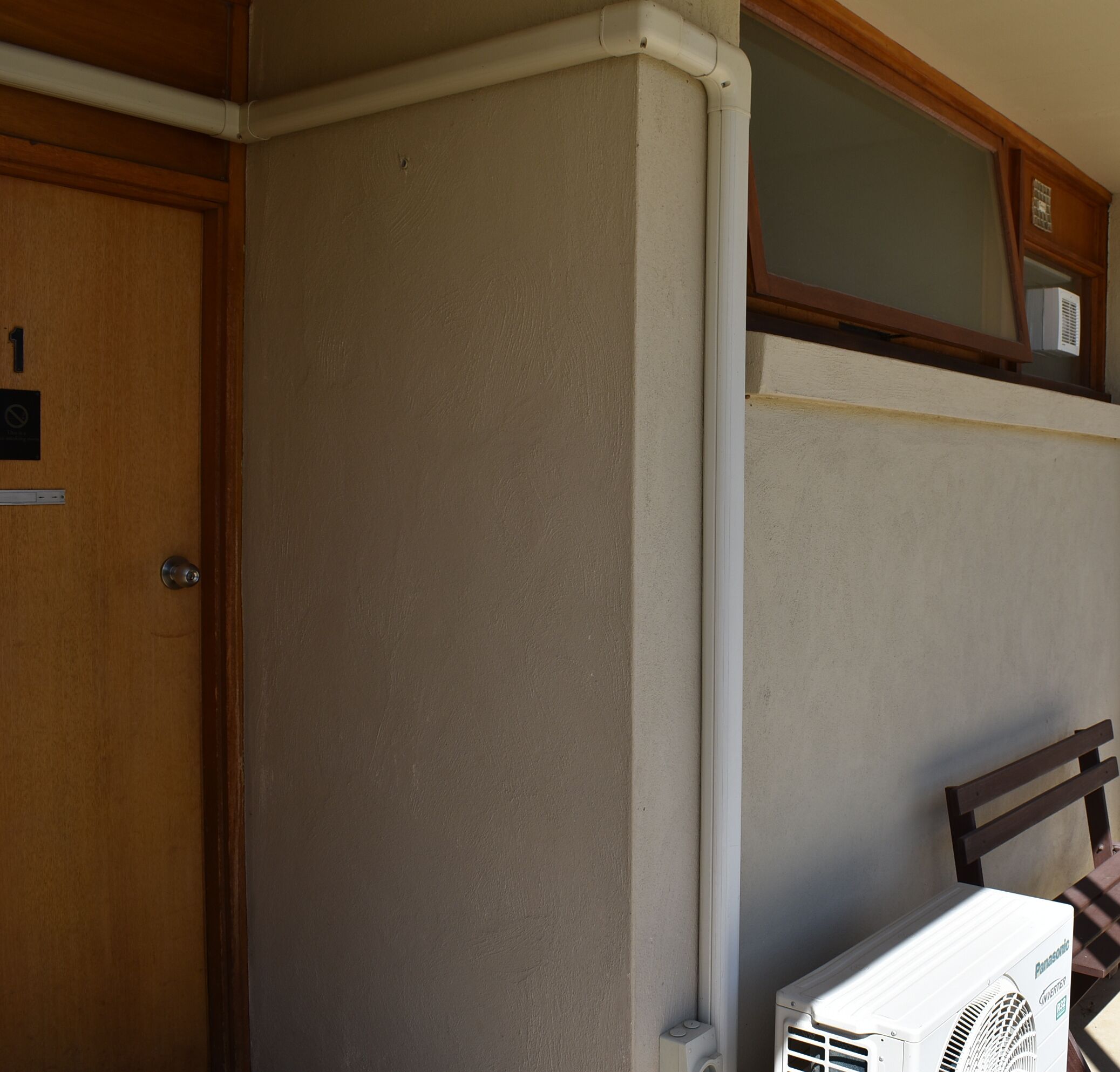 Una stanza con una porta in legno, un condizionatore d'aria bianco e una finestra con stipite in legno.