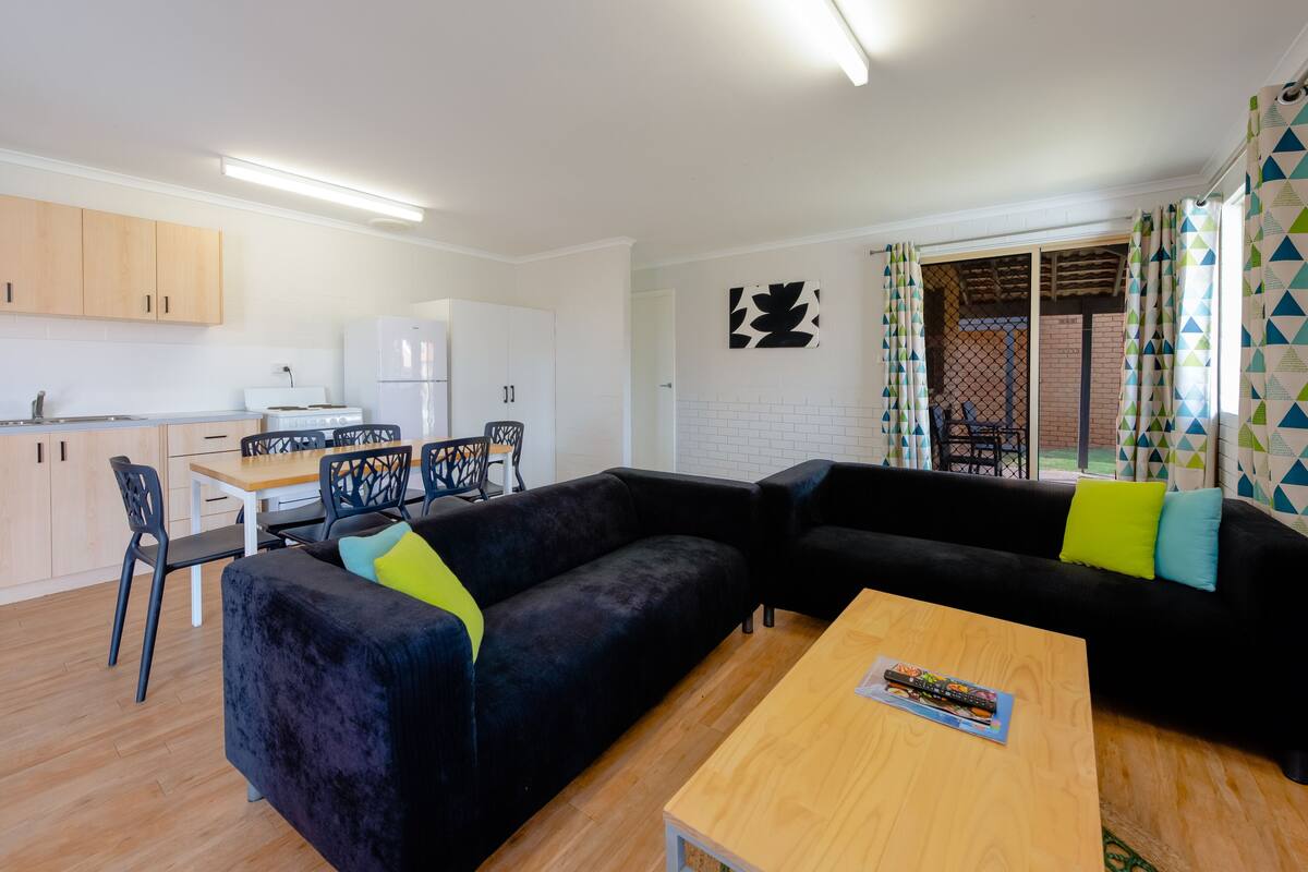 Una sala de estar moderna con un sofá negro, una mesa de centro de madera y una zona de comedor con mesa y sillas.