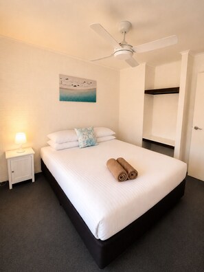 A hotel room with a bed, a ceiling fan, a nightstand with a lamp, a painting on the wall, and a bunk bed in the corner. - Geraldton's Ocean West (Mahomets Flats)