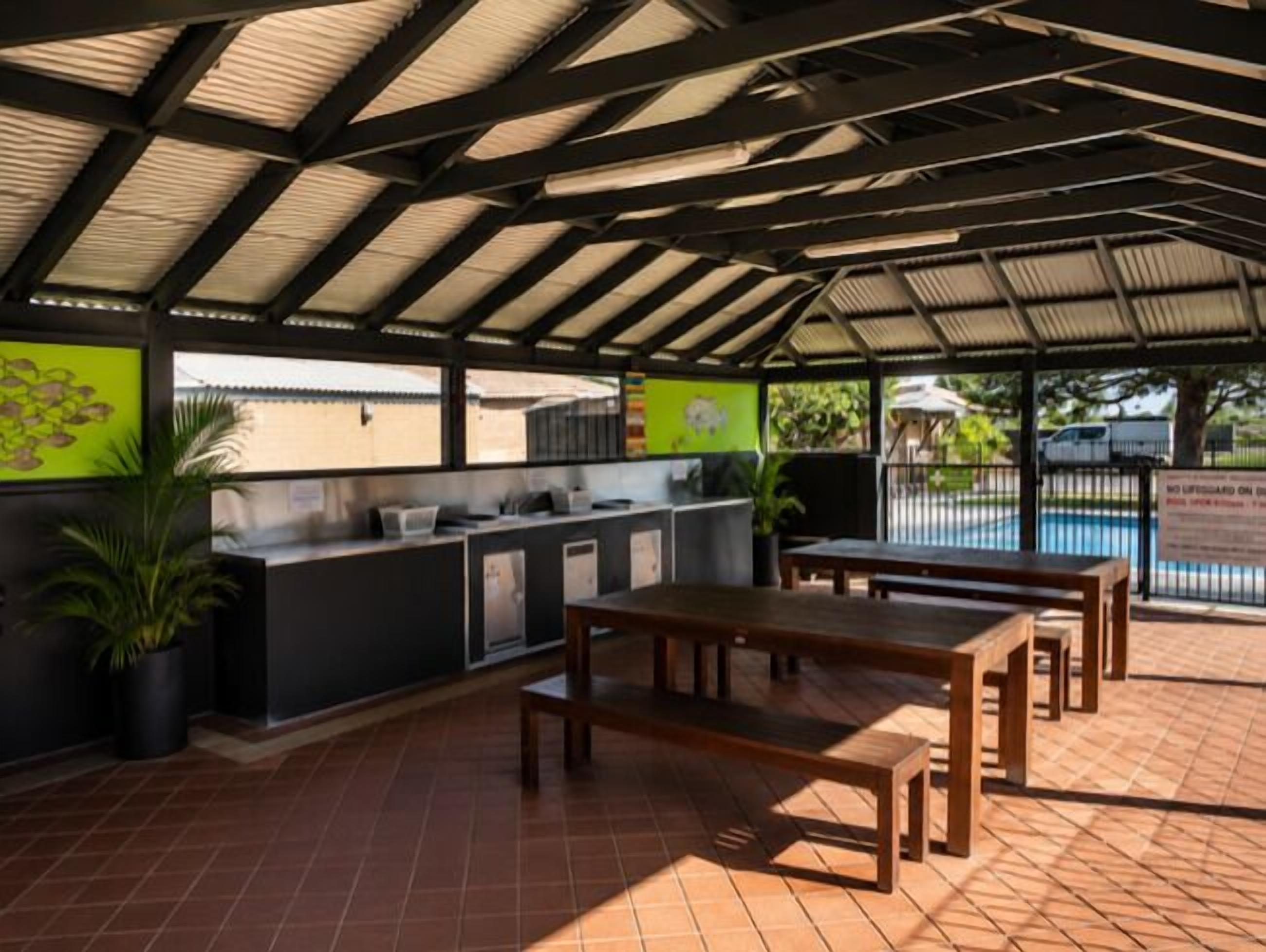 An outdoor patio with a dining area, a bar, and a pool in the background.