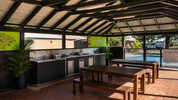 An outdoor patio with a dining area, a bar, and a pool in the background.