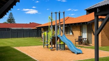 A playground with a slide and climbing structures, a fenced area, and a building with a red-tiled roof.