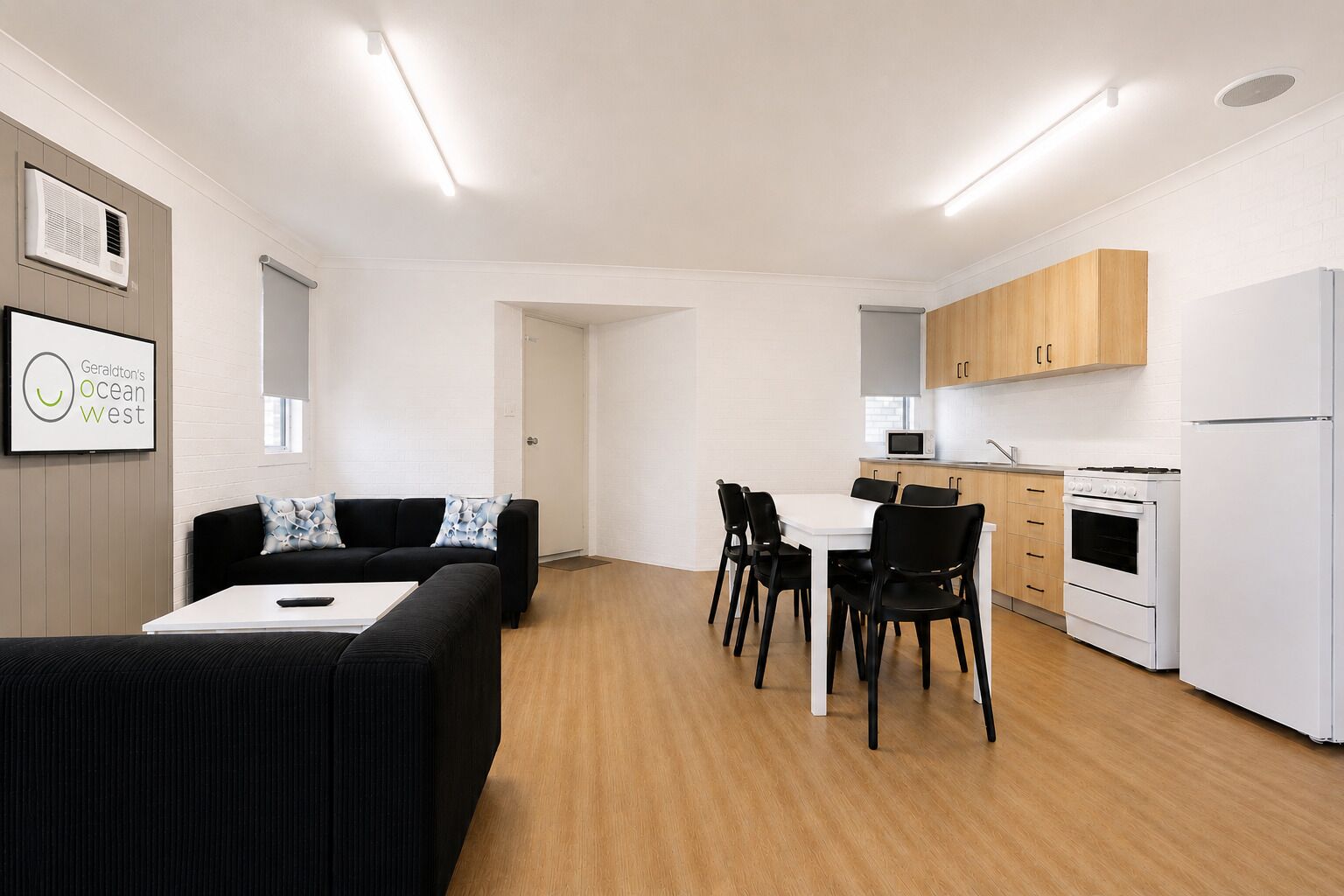 A modern kitchen with white cabinets, a microwave, stove, and a refrigerator. There is a dining area with a white table and black chairs.