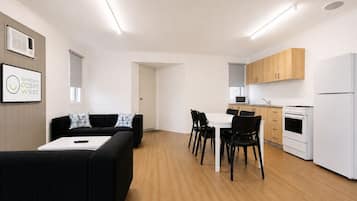 Une cuisine moderne avec des meubles blancs, un four à micro-ondes, une cuisinière et un réfrigérateur. On y trouve également un coin repas avec une table blanche et des chaises noires.