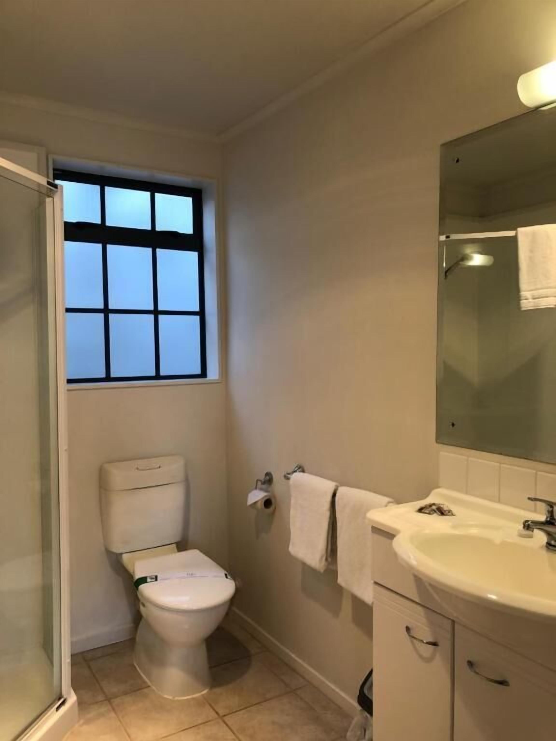 A bathroom with a toilet, a sink, a mirror, and a window.