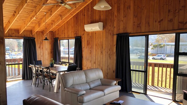 A cozy room with a wooden ceiling, a leather sofa, a dining table with chairs, and large windows with curtains.