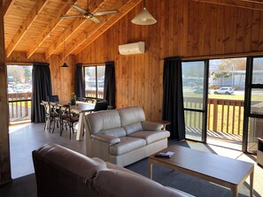 A cozy room with a wooden ceiling, a leather sofa, a dining table with chairs, and large windows with curtains. - Alpine Motel (Ohakune)