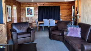A cozy room with wooden walls, a dining area with a table and chairs, and leather sofas.