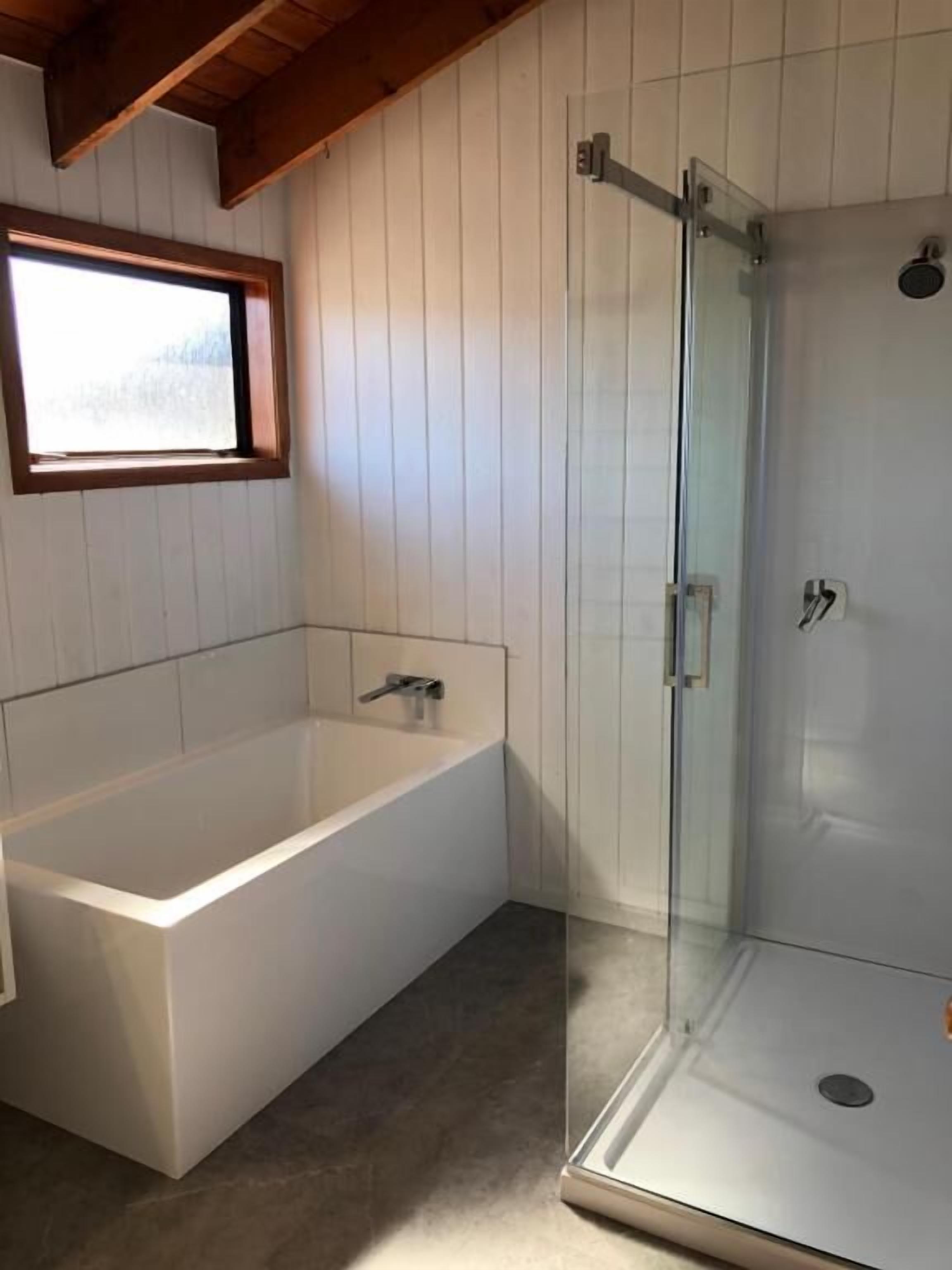 Ein Badezimmer mit einer Badewanne, einer Duschkabine aus Glas und einem Fenster.