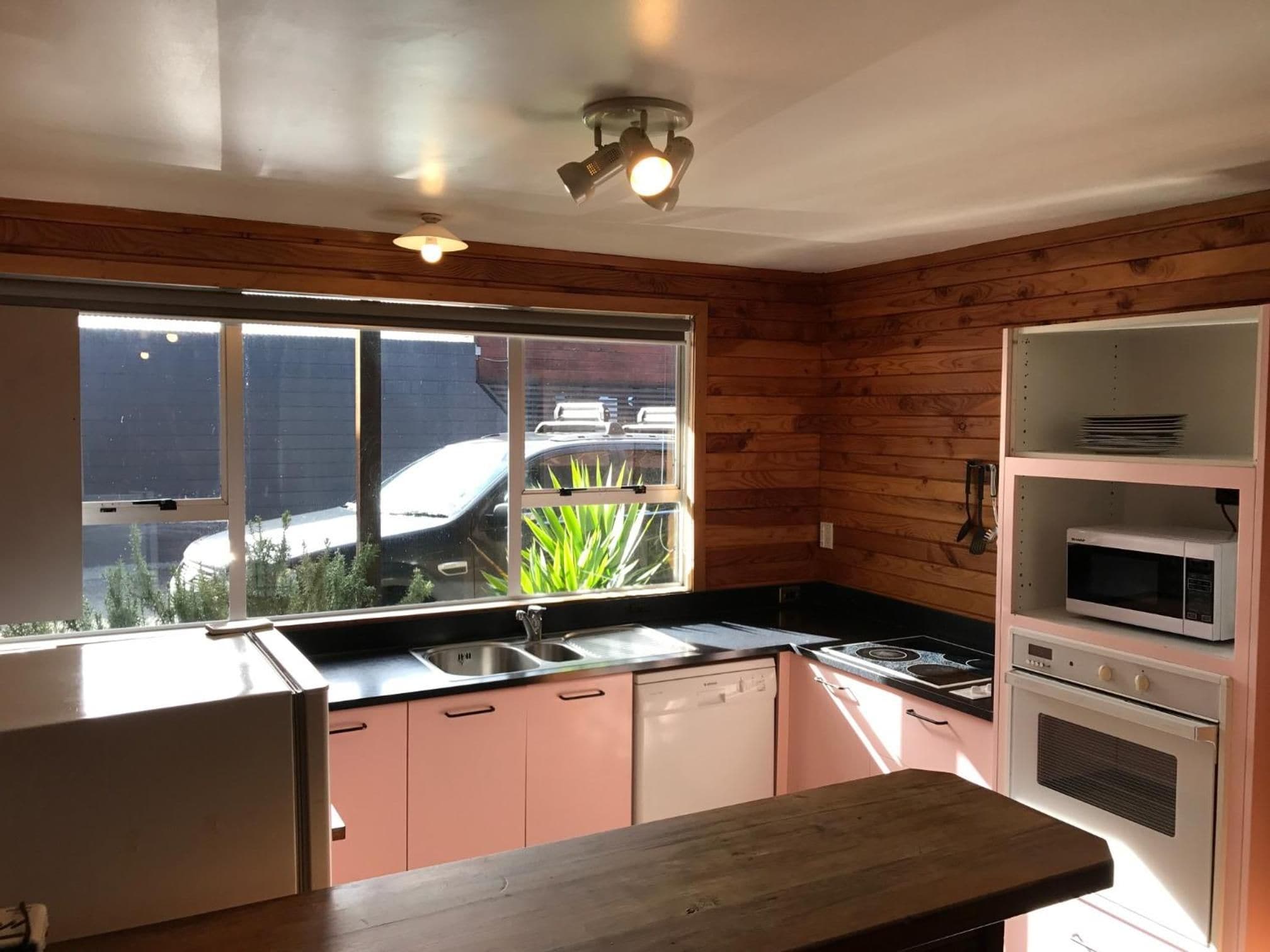 A kitchen with wooden walls, a window with a view, a sink, a stove, and a microwave.