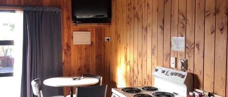A wooden-paneled kitchen with a stove, sink, and a flat-screen TV mounted on the wall.