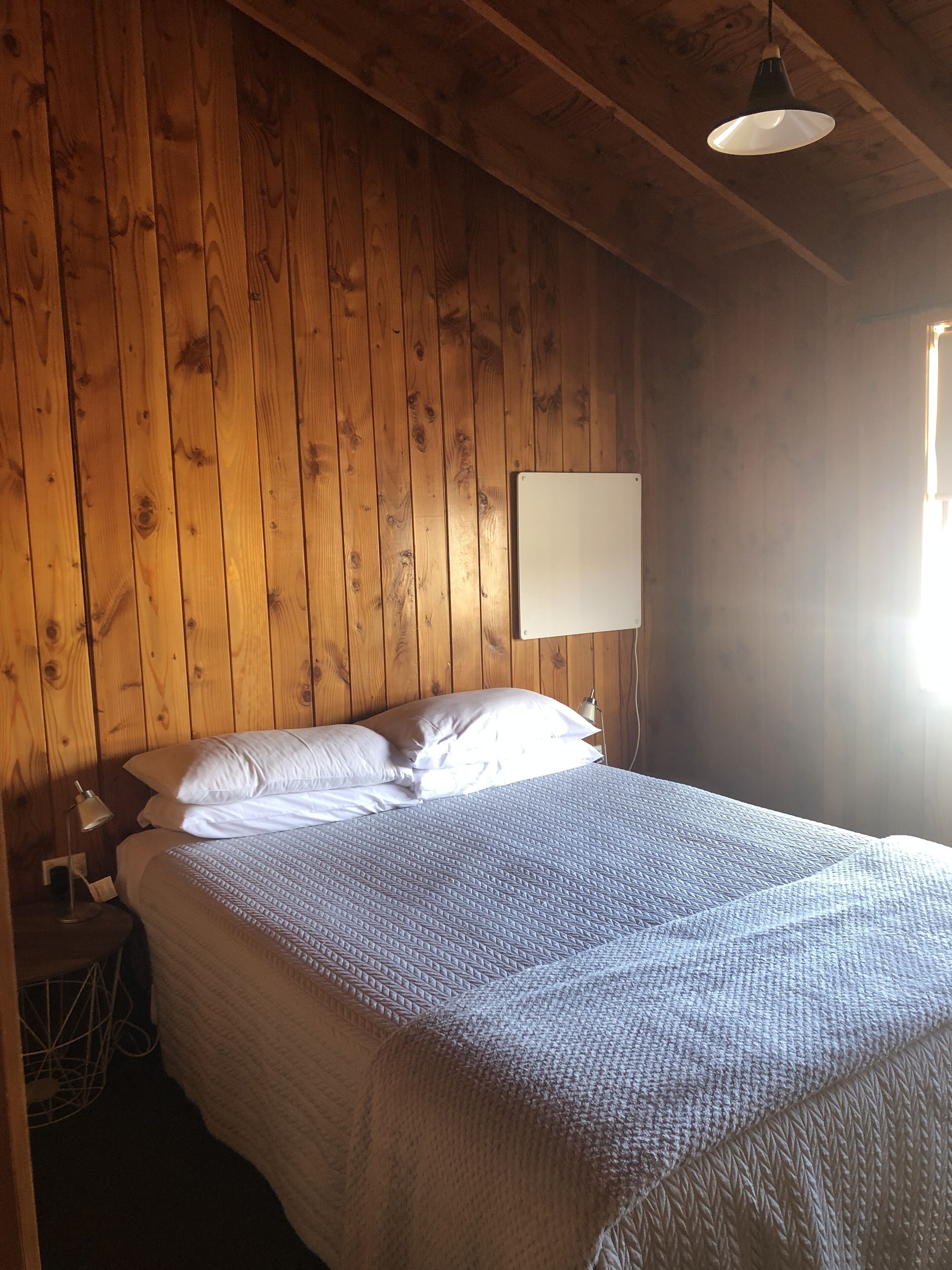 A wooden-paneled room with a bed, a nightstand, and a window.