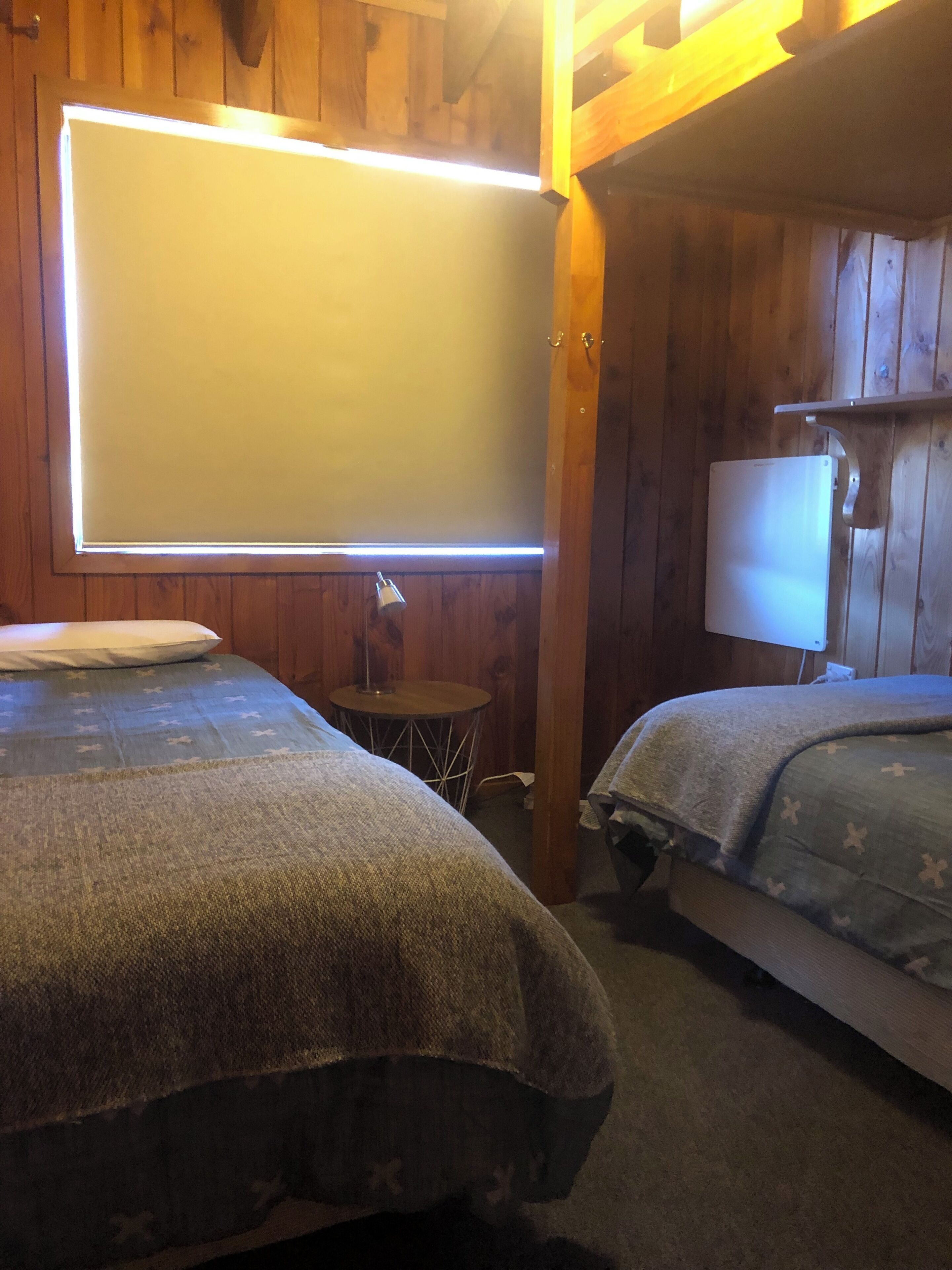 Una habitación con dos camas, una mesita y una lámpara en la pared.