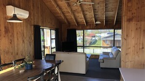 A cozy cabin interior with a wooden ceiling, a dining area with a table and chairs, a sofa, and a television.