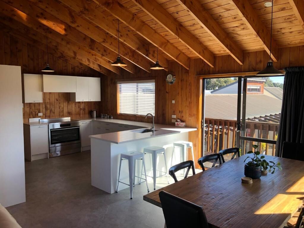A modern kitchen with white cabinets, a central island with bar stools, and a dining area with a wooden table.