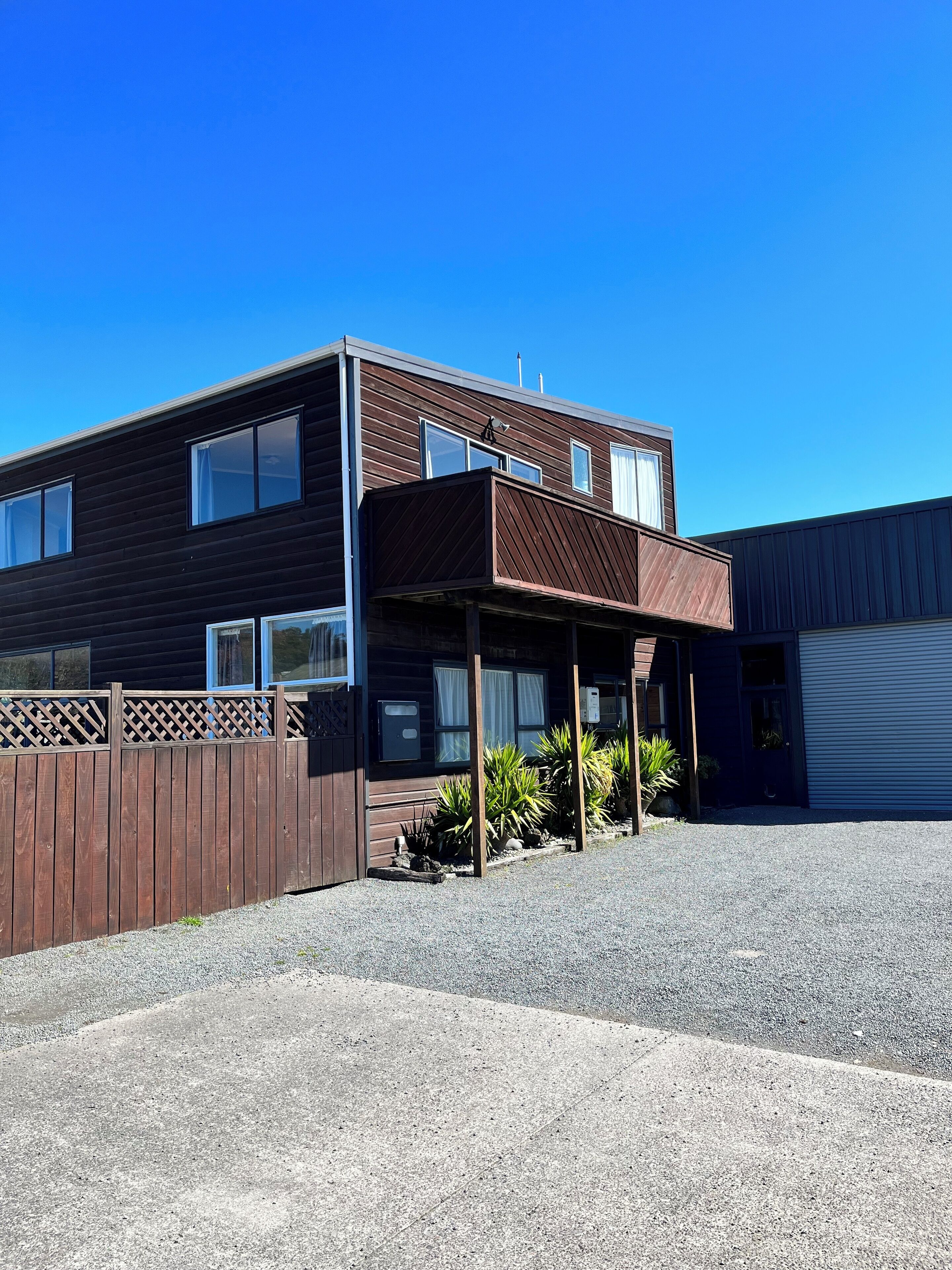 A two-story building with a wooden facade, a covered porch, and a gravel driveway.