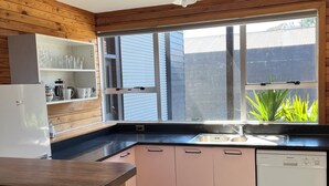 A modern kitchen with wooden paneling, a built-in shelf with glassware, a stainless steel sink, and a dishwasher.