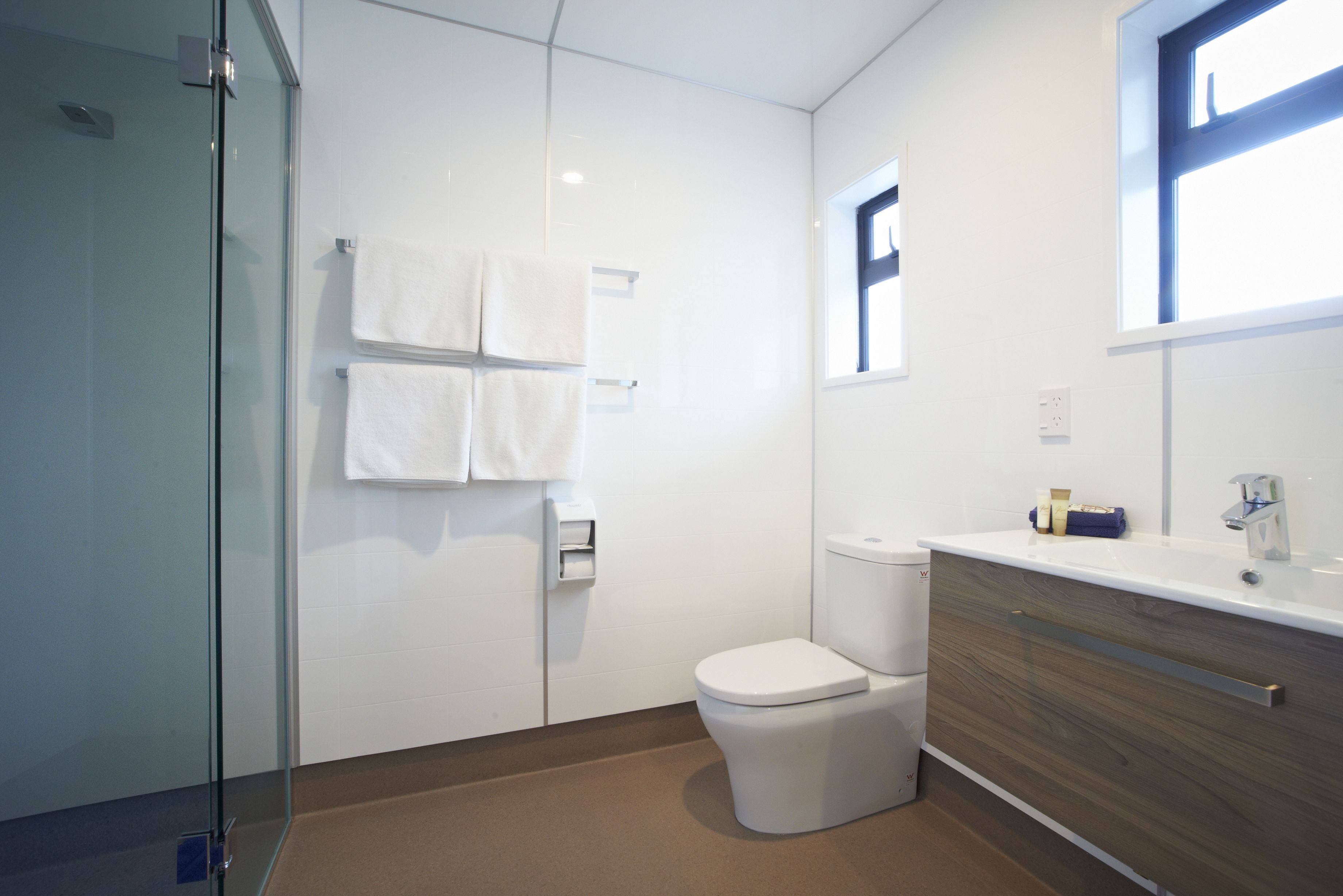 Un baño moderno con cabina de ducha de vidrio, inodoro blanco y tocador de madera con espejo.