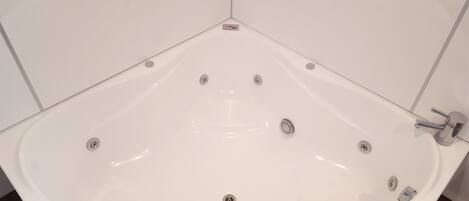 A corner bathtub with a built-in showerhead and multiple faucets.