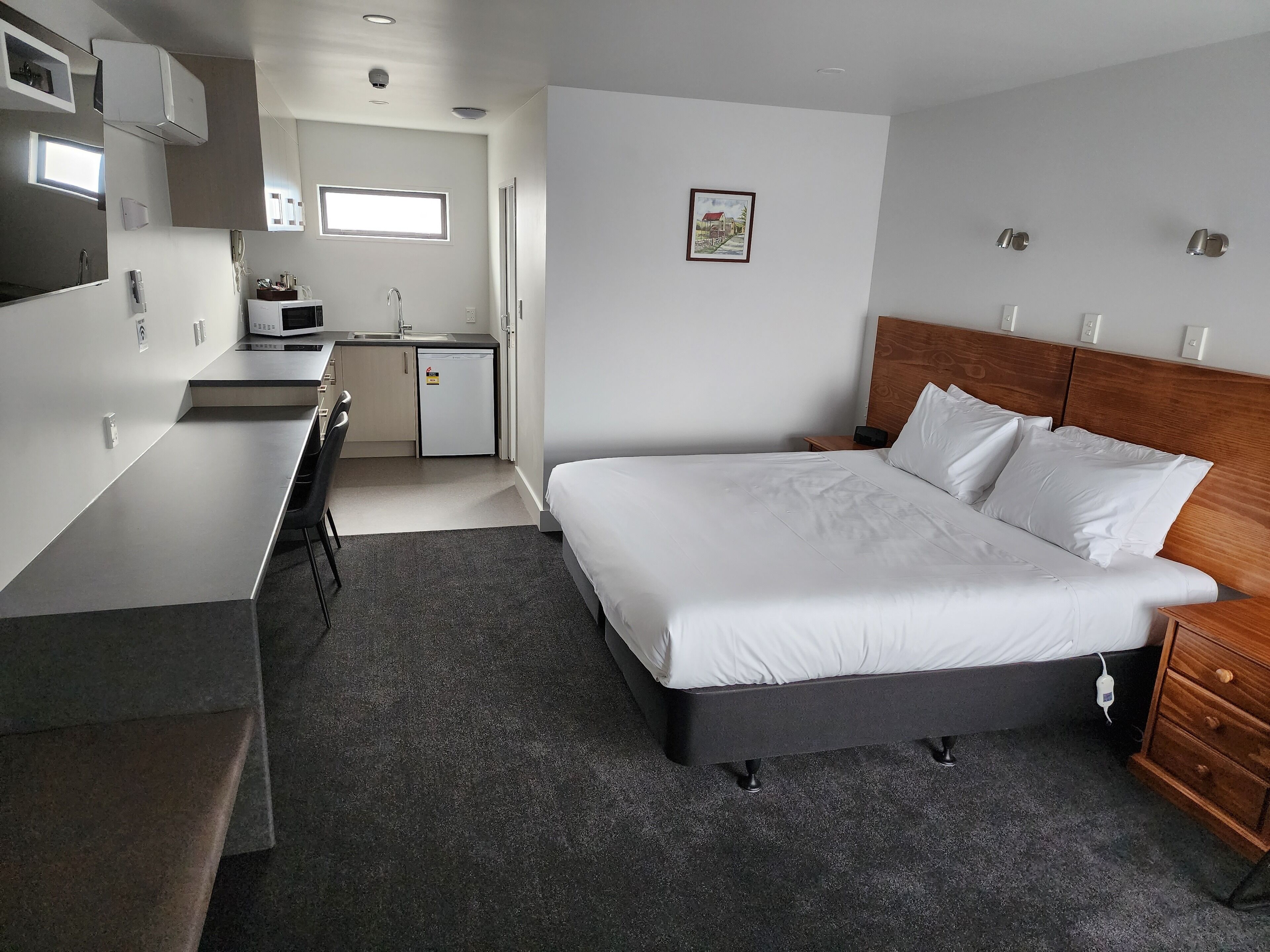 Une chambre d’hôtel de taille réduite, comprenant un lit, une table de chevet et une petite kitchenette.