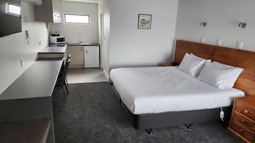 Habitación de hotel pequeña con cama, mesita de noche y una kitchenette.