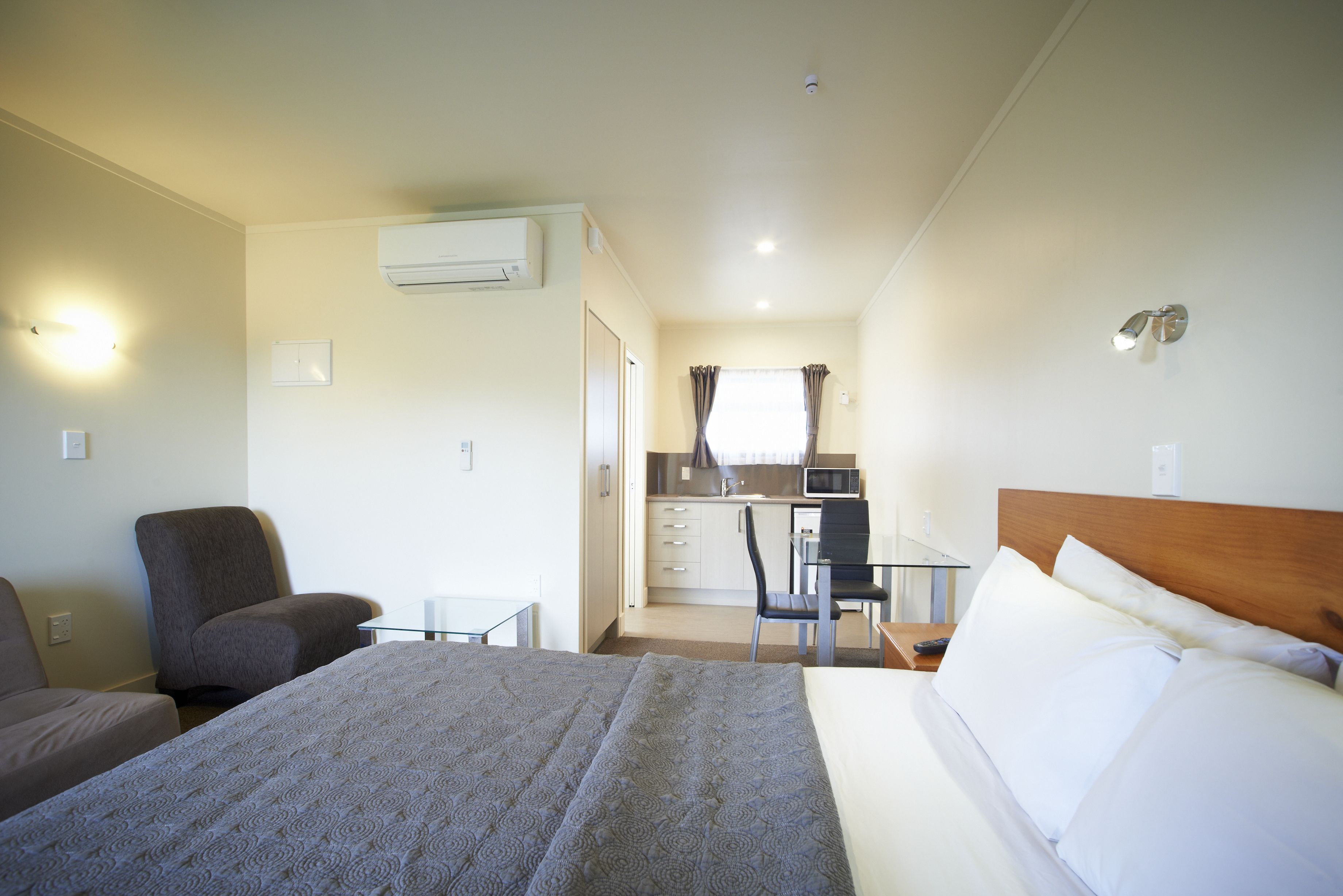 Una habitación de hotel con cama, una silla, escritorio y kitchenette.