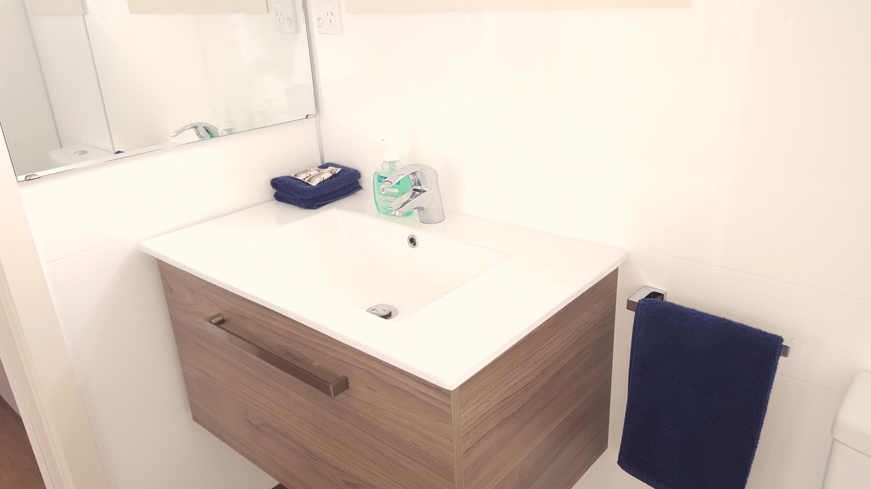 Un baño con lavamanos blanco, tocador de madera, un espejo y una toalla azul.