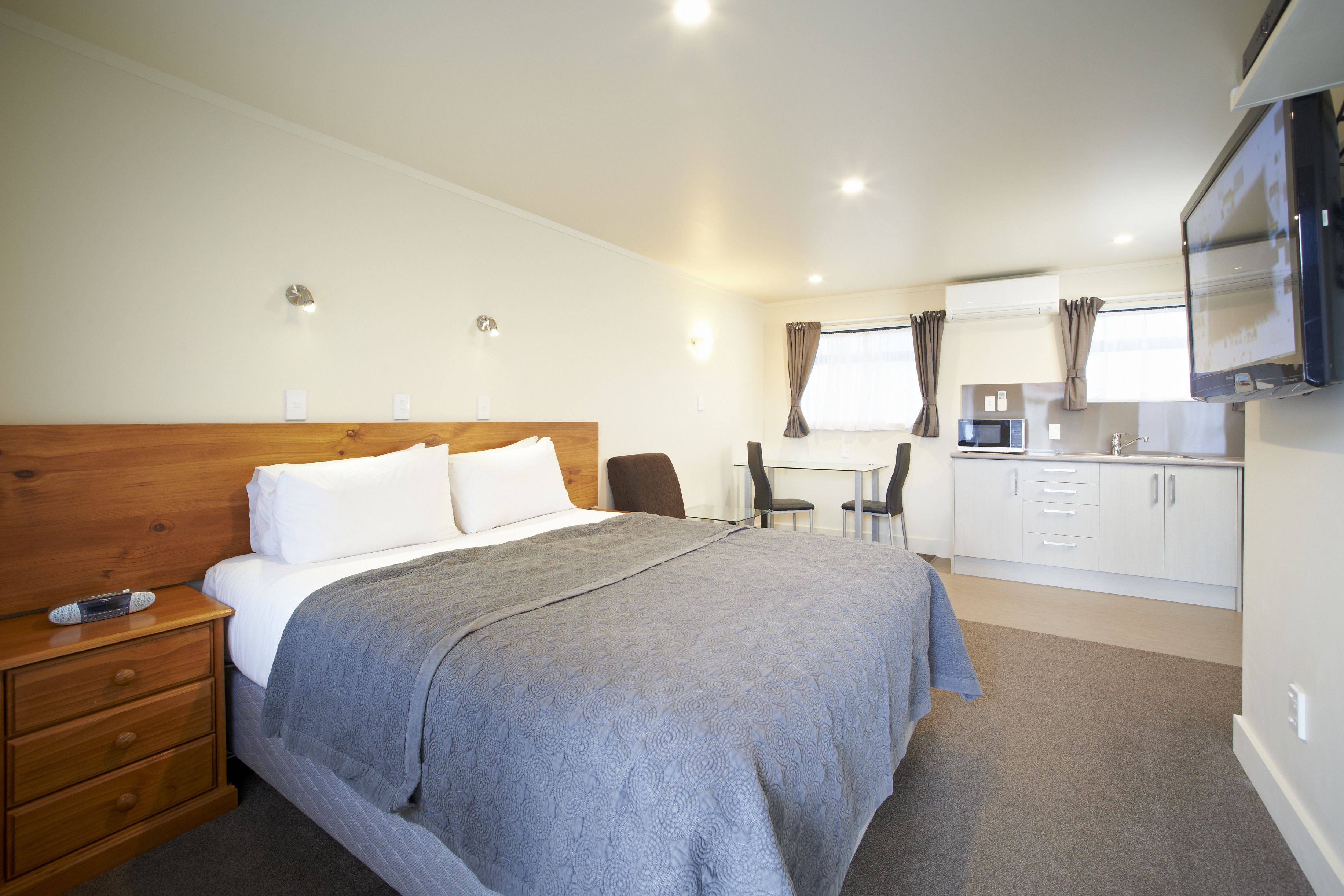 Een slaapkamer met een bed, nachtkastje en een aan de muur bevestigde televisie.