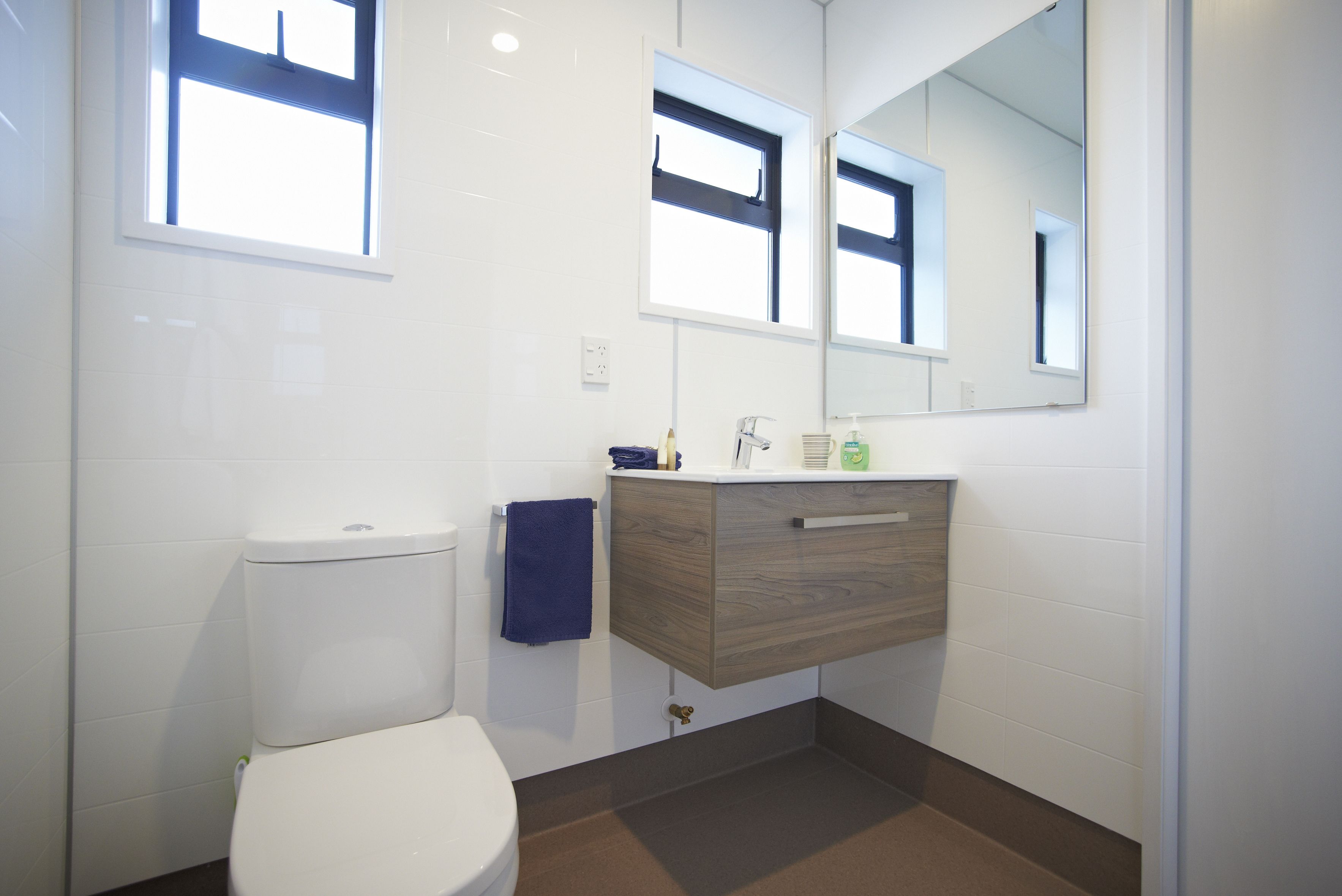 Un baño moderno con inodoro blanco, tocador de madera, espejo y ventana.