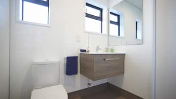 Un baño moderno con inodoro blanco, tocador de madera, espejo y ventana.