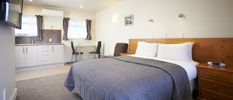 A bedroom with a large bed, a wooden headboard, a bedside table, and a nightstand. There is a small desk with a chair and a window with curtains.