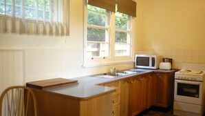 Una cocina con armarios de madera, estufa, microondas y una ventana con persianas.