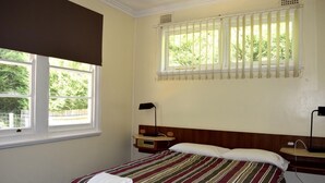 Habitación de hotel con cama, mesita de noche, ventana con persianas y vista a zonas verdes.