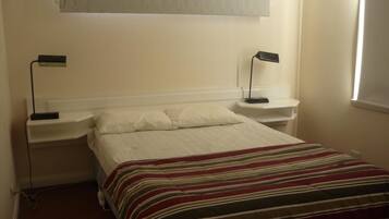 A simple, clean bedroom with a bed, two bedside tables, and a window with blinds.