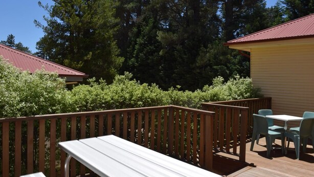Una terraza con barandilla de madera, una mesa blanca y dos sillas azules.