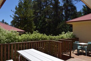 A deck with a wooden railing, a white table, and two blue chairs. - Blackheath Holiday Cabins (Blackheath)