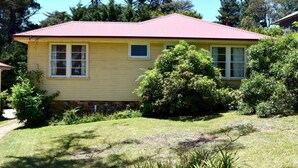 Una casa amarilla con techo rojo, rodeada de follaje y árboles.