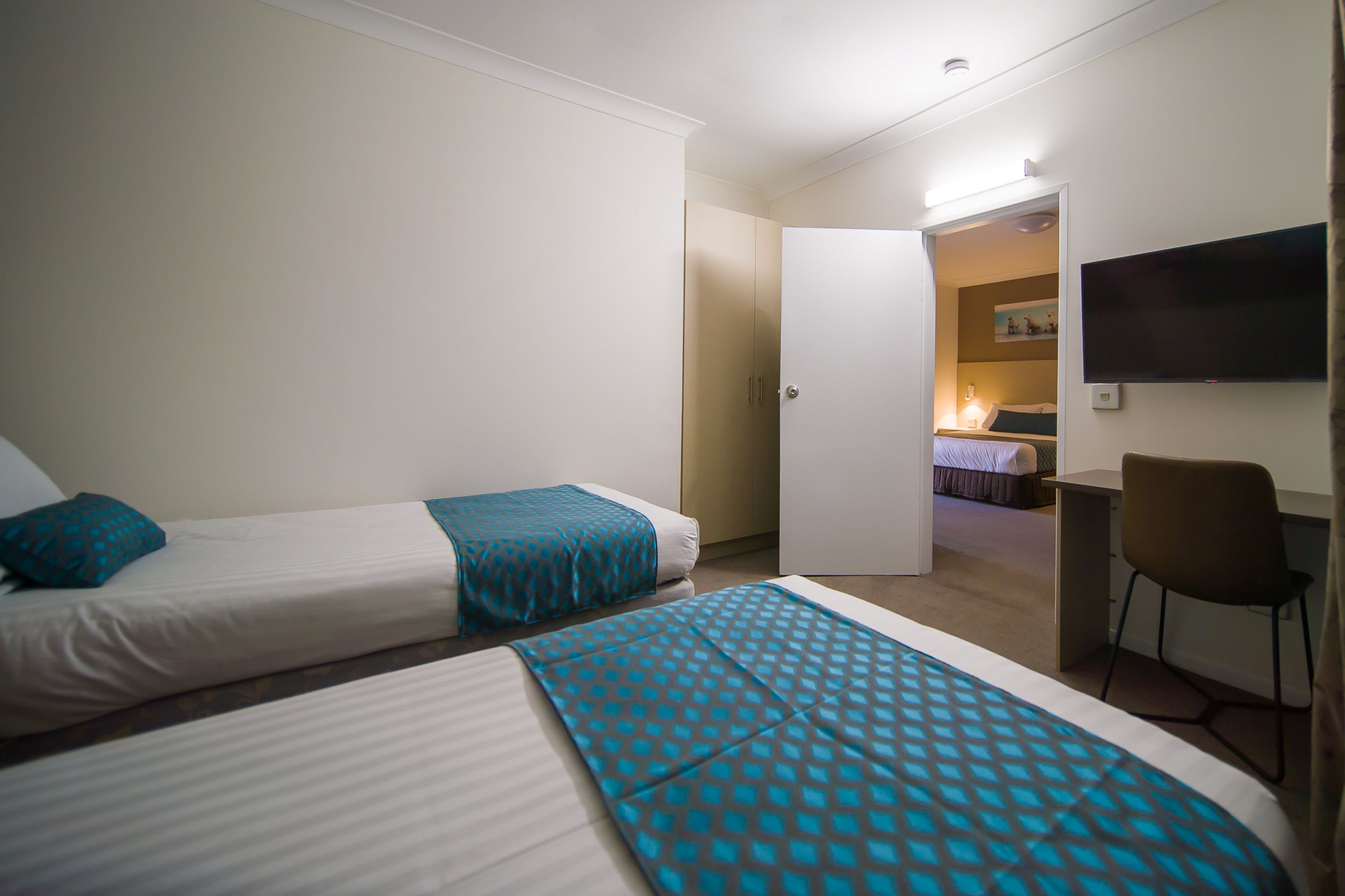 Una habitación de hotel con dos camas, un escritorio, una silla y un televisor en la pared.