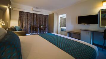 Ett hotellrum med en stor säng, ett skrivbord, en stol, en tv och ett fönster med gardiner.