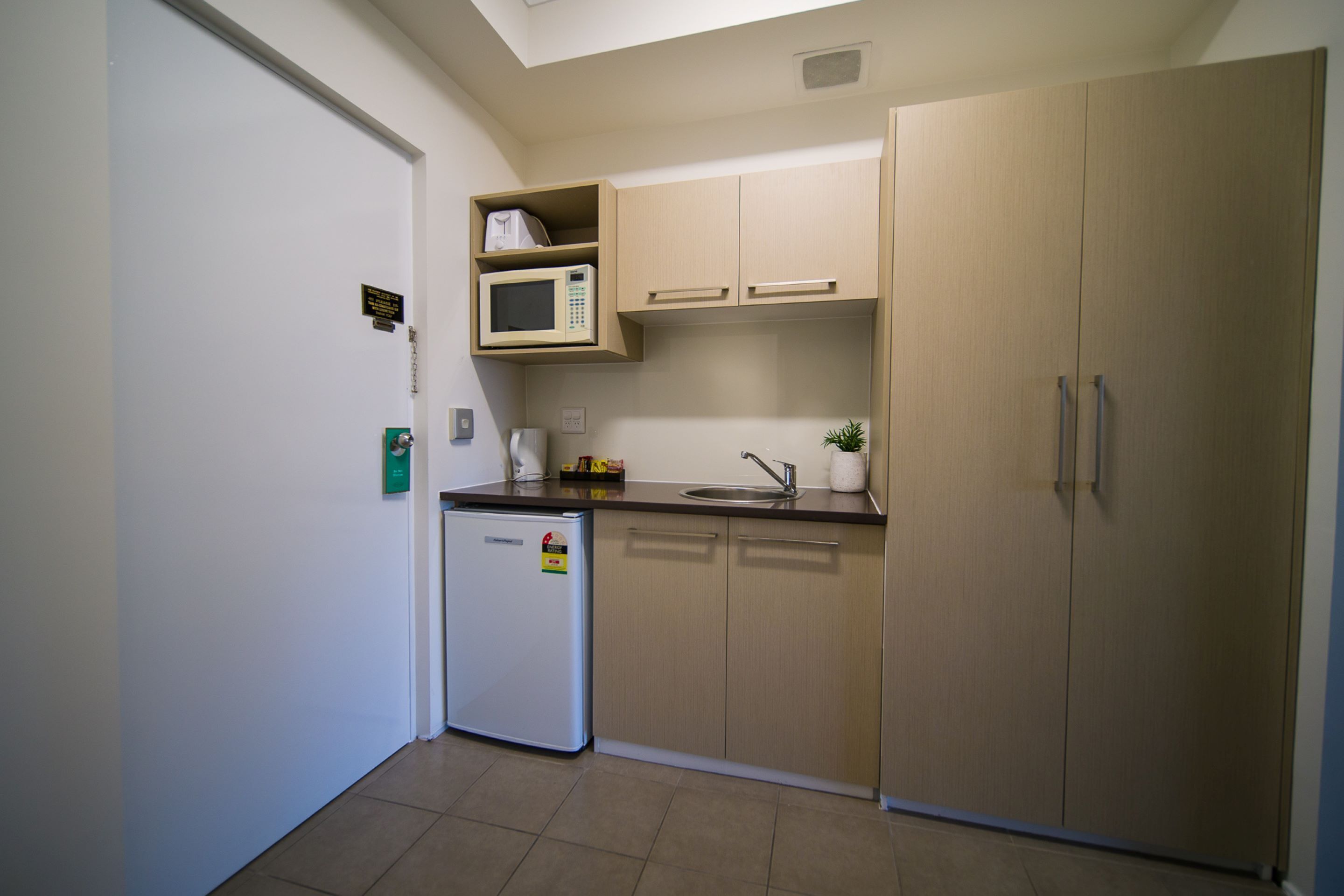 A compact kitchen with a refrigerator, microwave, sink, and wooden cabinets.