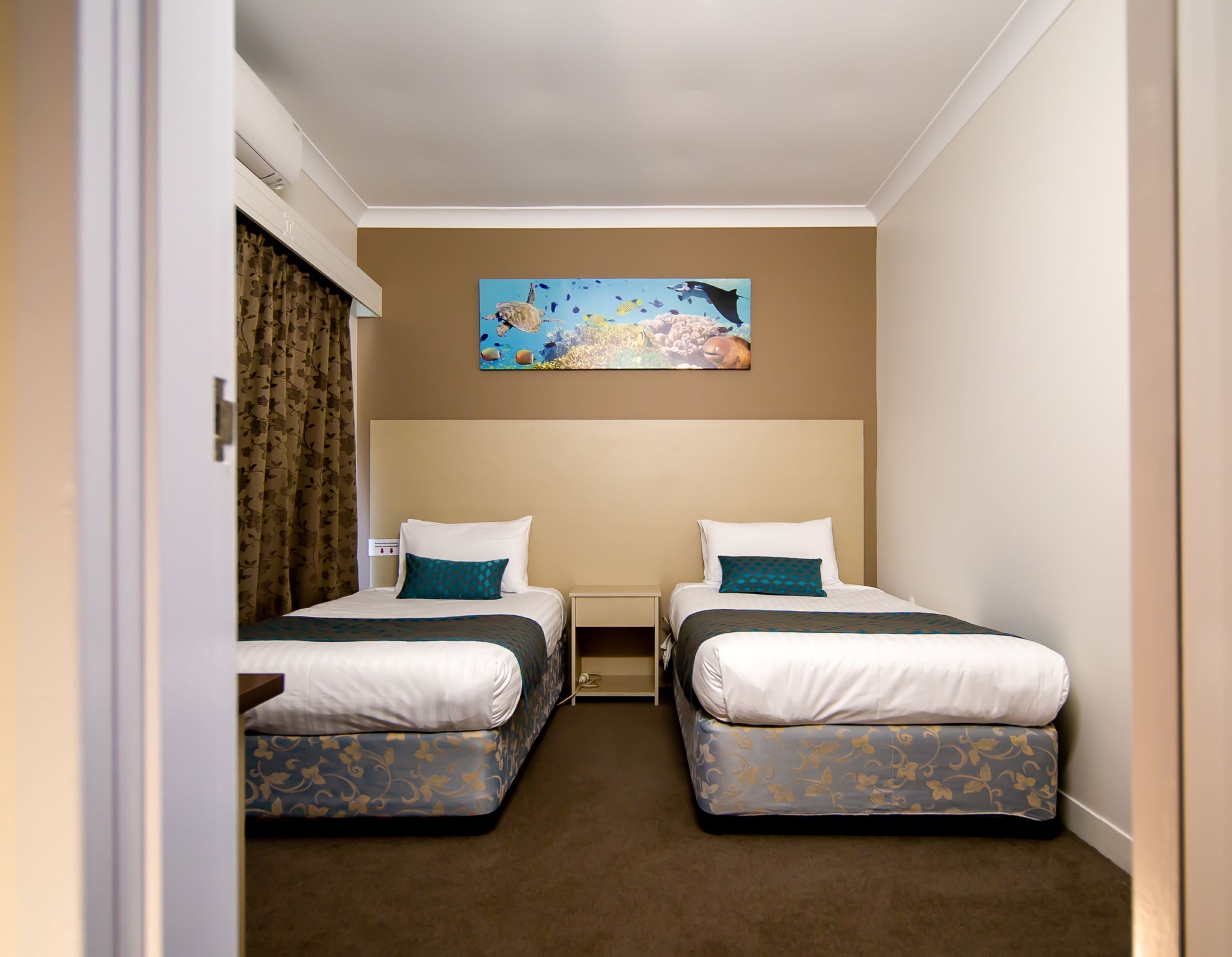 Habitación de hotel con dos camas, un cuadro en la pared y suelo cubierto de alfombra.