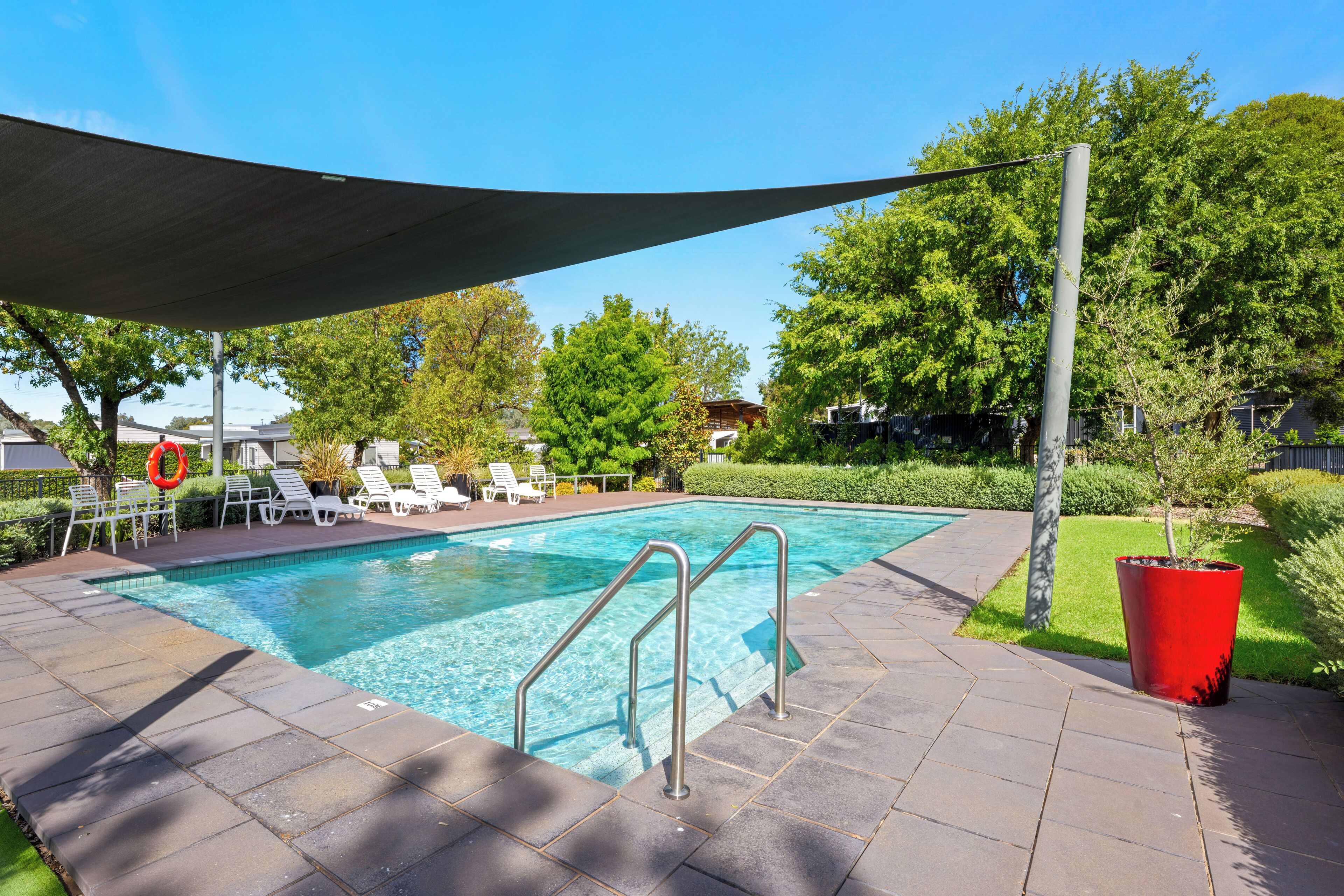 A swimming pool with clear water, surrounded by lounge chairs and a shaded area.
