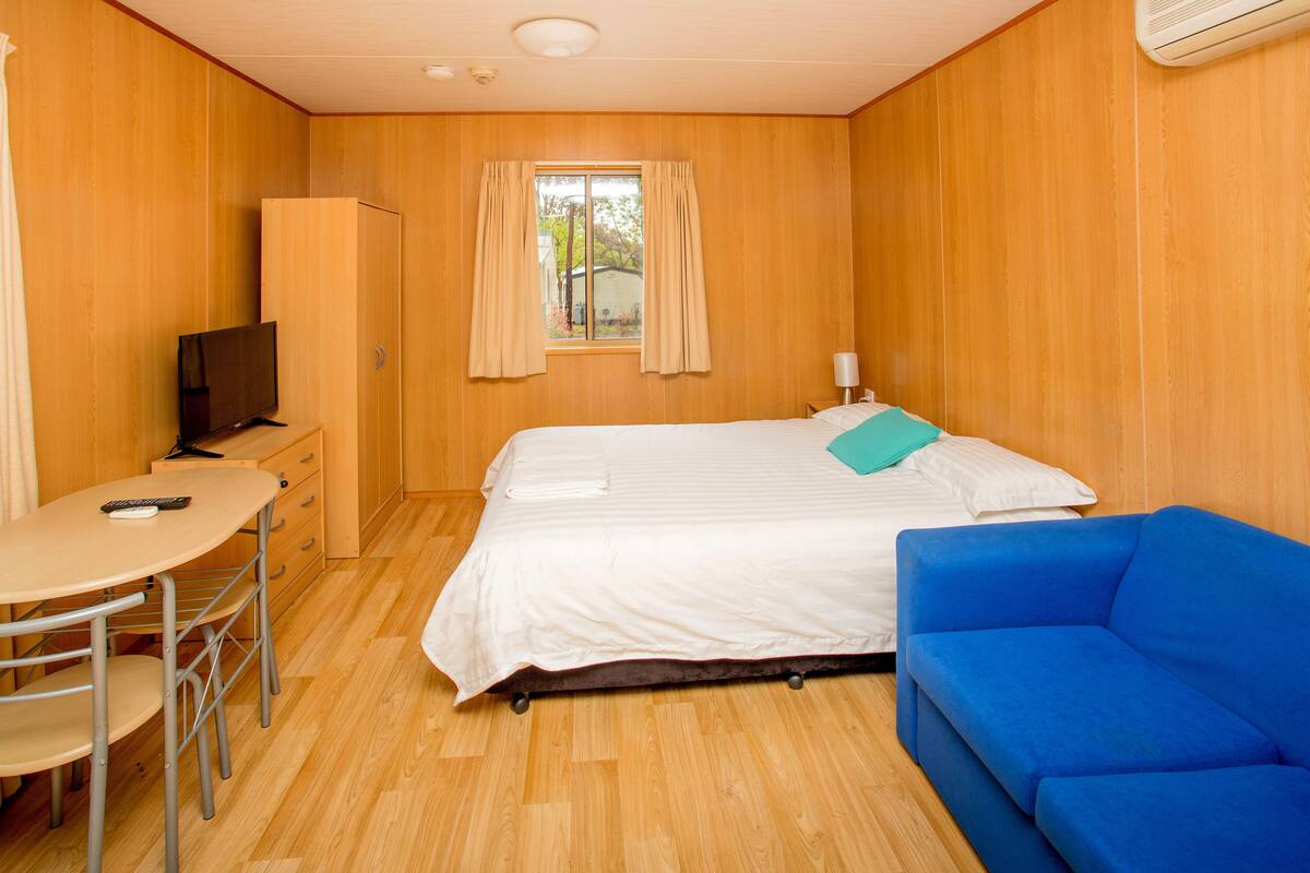 Une pièce comprenant un lit, un canapé bleu, une télévision, un bureau et une armoire.