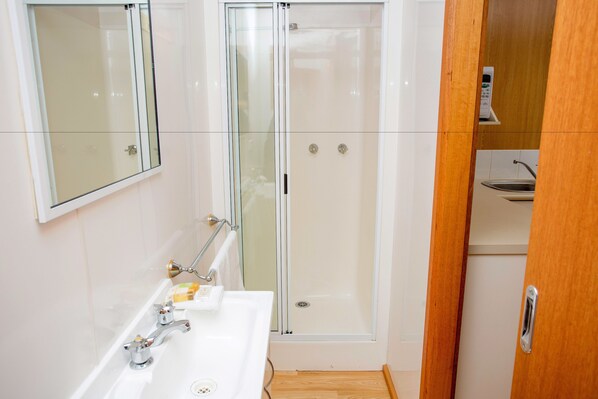 A modern bathroom with a glass-enclosed shower, a white sink with a soap dispenser, and a wooden cabinet. - Albury Gardens Tourist Park (Lavington)