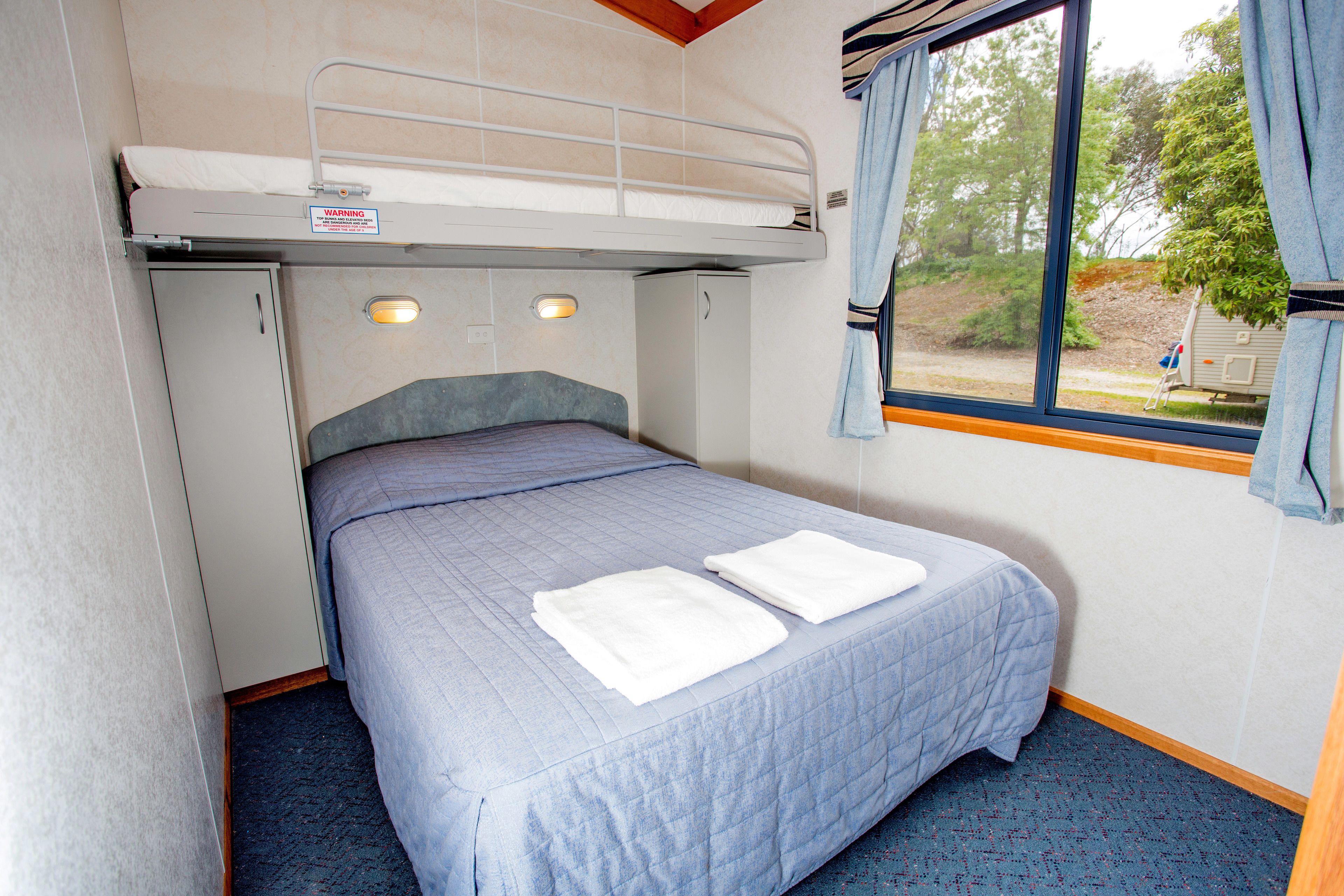 A bunk bed with a headboard, a window with curtains, and a bed with two white towels.