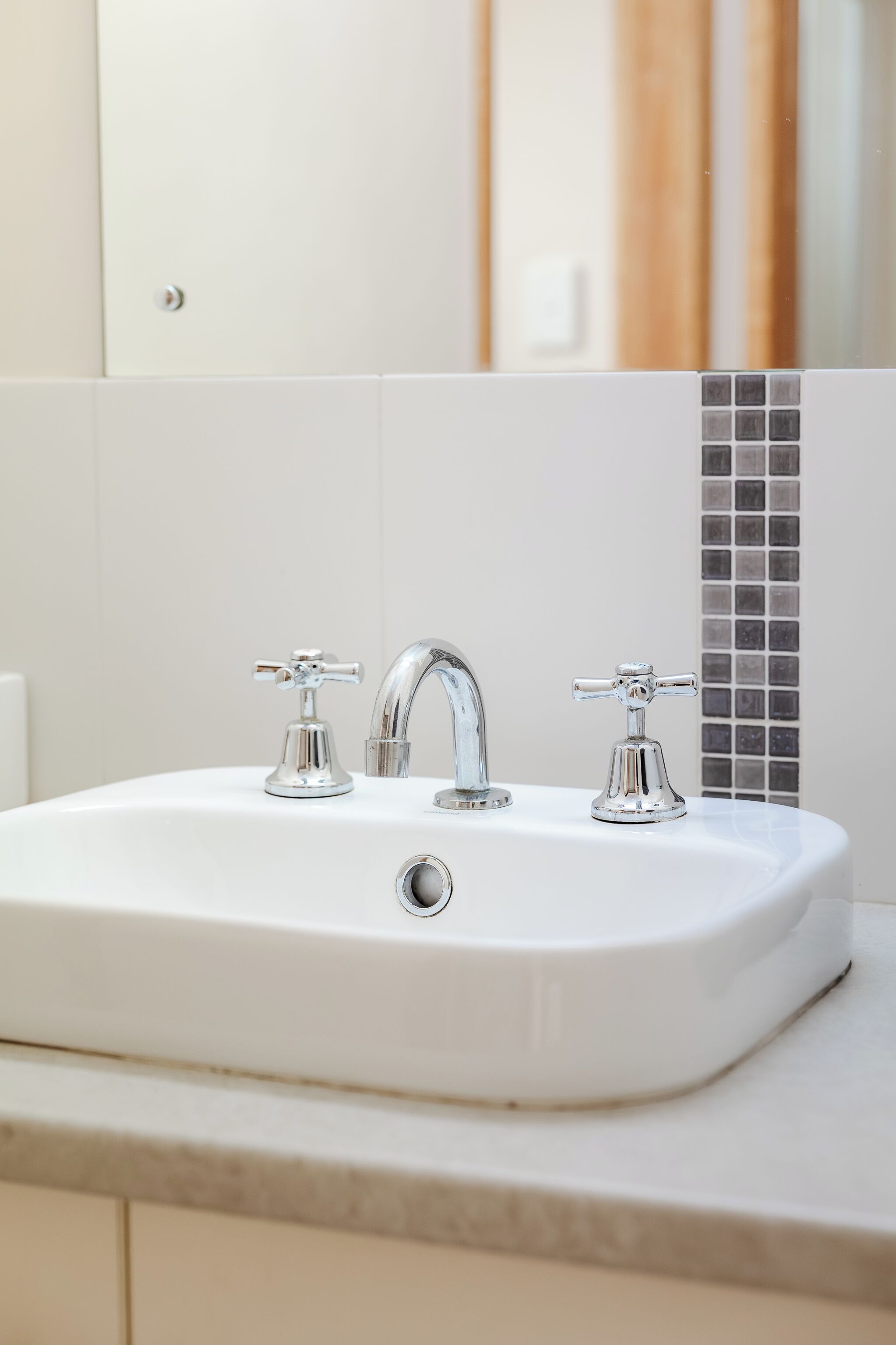 A bathroom sink with two faucets and a tiled backsplash.