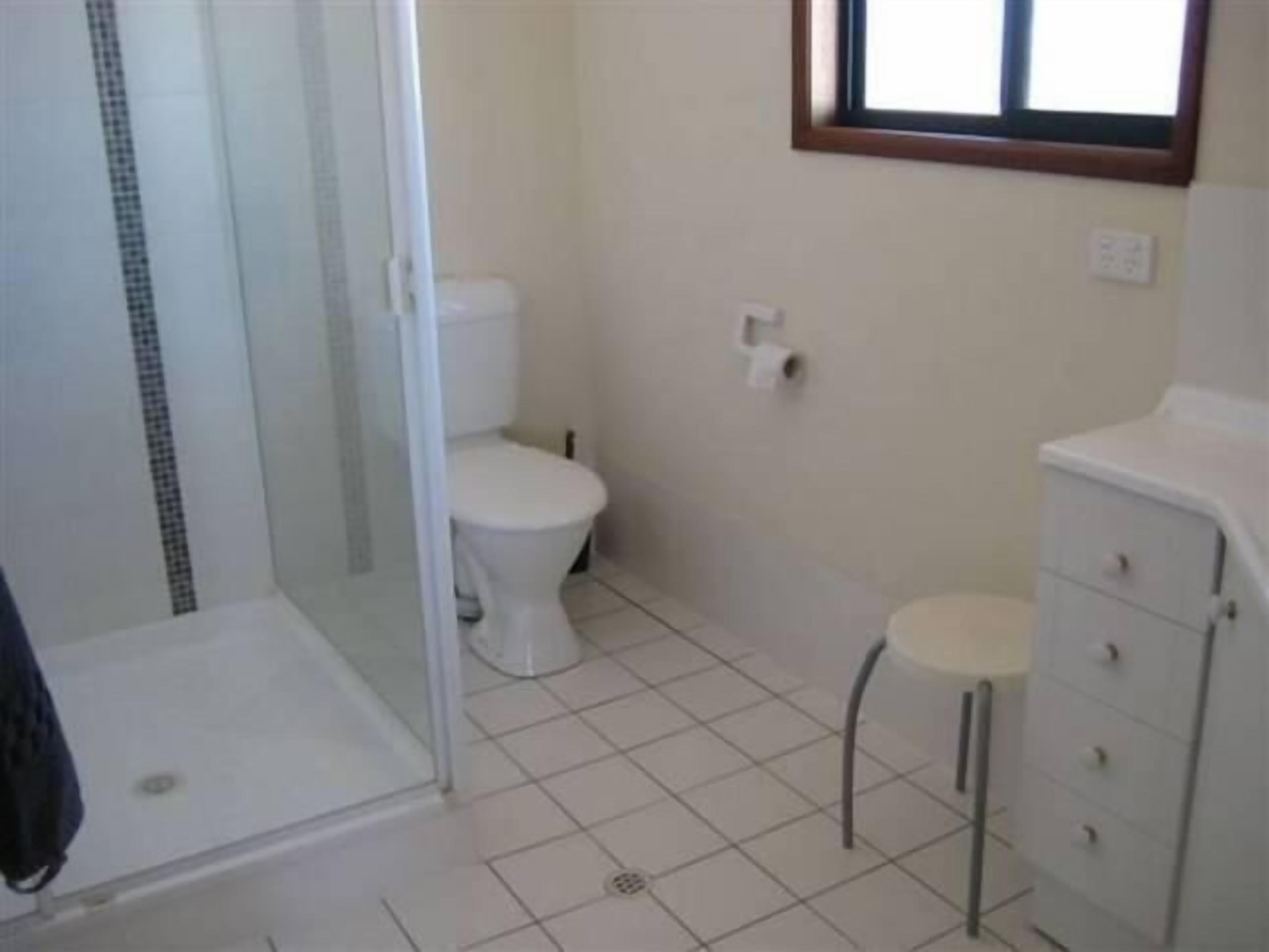 A bathroom with a glass shower enclosure, a toilet, a small stool, and a cabinet.