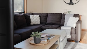 A modern living room with a sectional sofa, a flat-screen TV, a coffee table with a plant, and a decorative wall piece. - Waves and Wildlife (Stokes Bay)